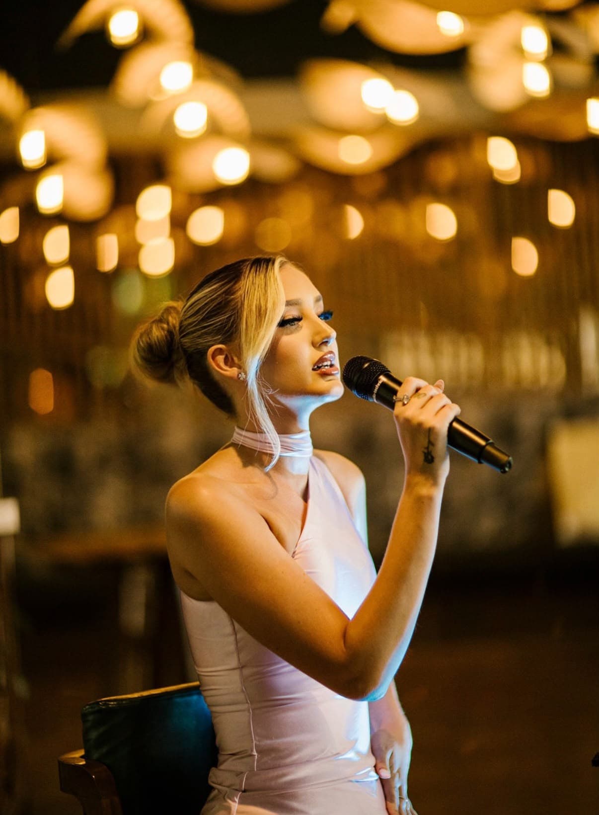 Dannii Murphy singing at an evening event beneath warm hanging lights
